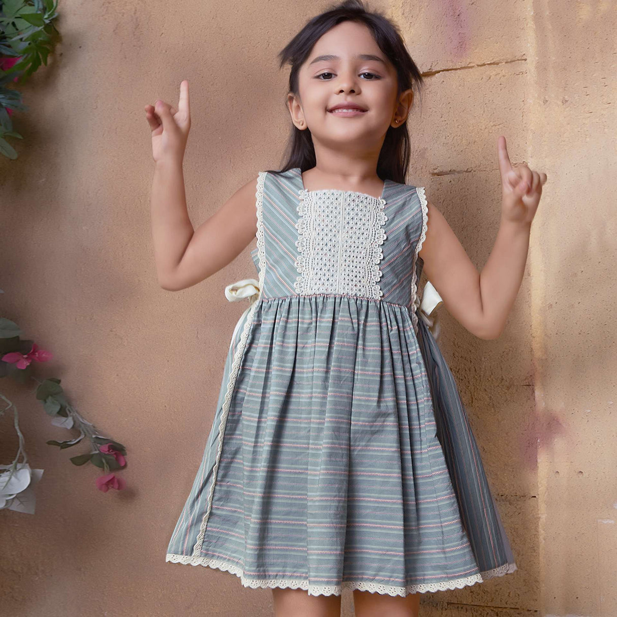 A young girl showcasing striped sleeveless dress with charming side bows and delicate lace trims