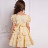 Back view of a girl wearing an ivory beads dress with a tie-up sash, fastened by buttons