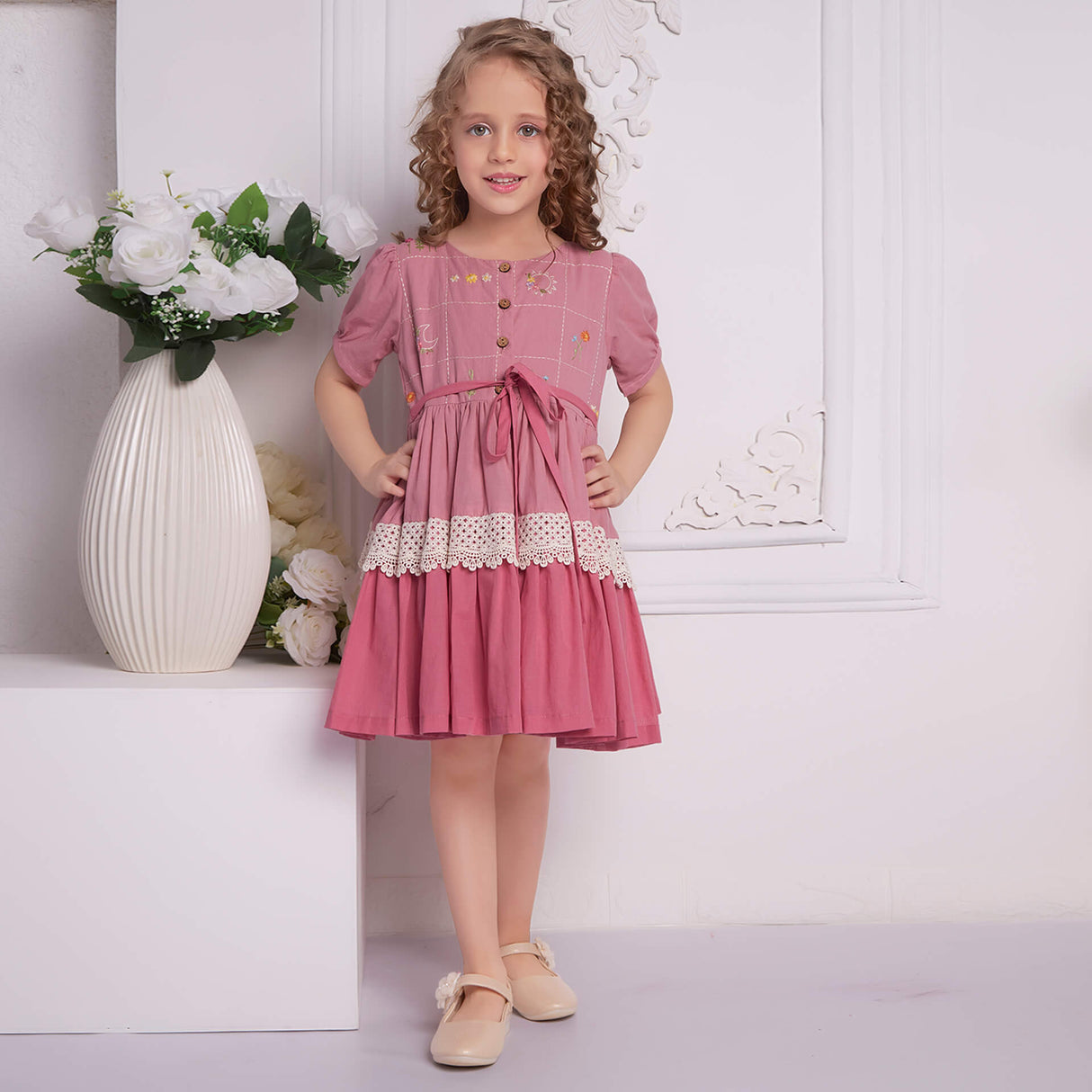 With hands on hips, a young girl posing in a pink ombre embroidered dress