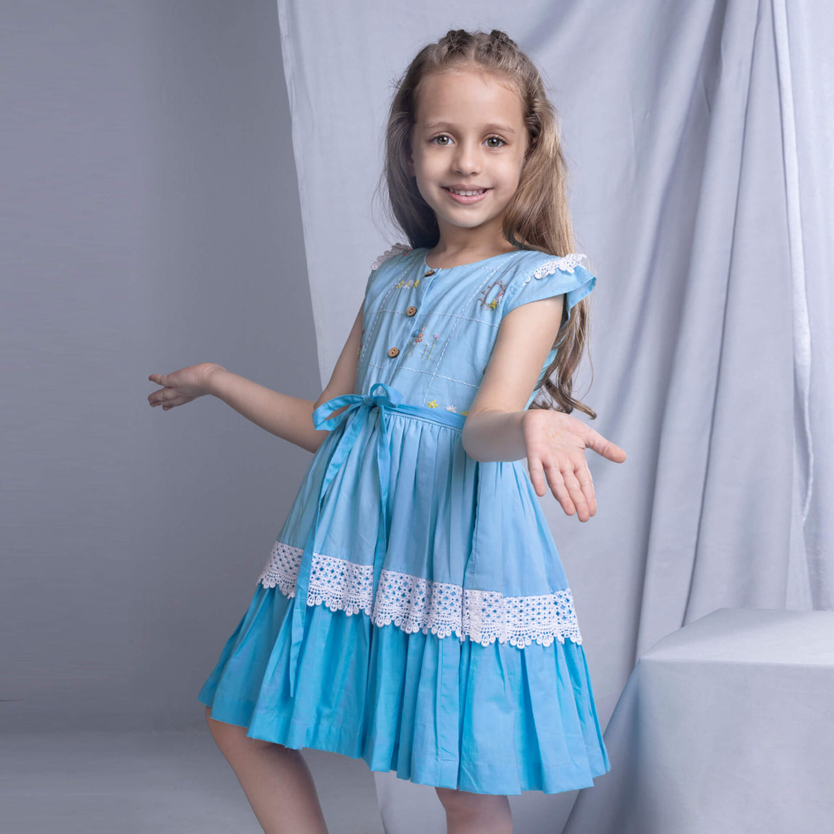 A side view of a young girl in a blue ombre dress, showcasing delicate embroidery and lace details