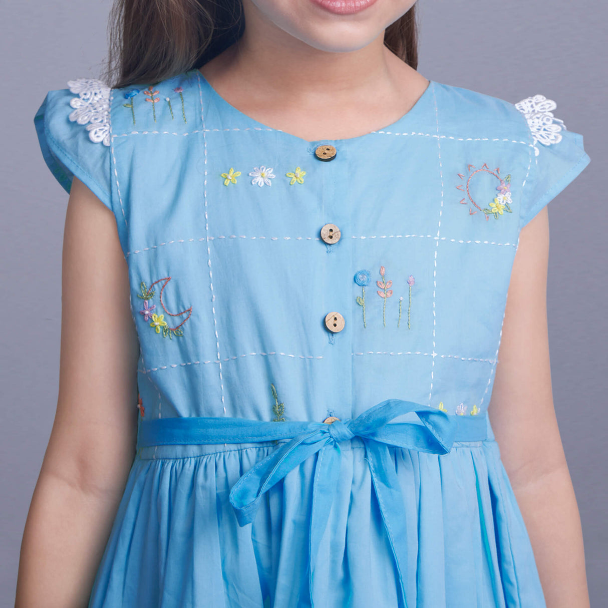 Closeup of hand embroidery on a blue ombre dress with front wood buttons and a tie-up sash