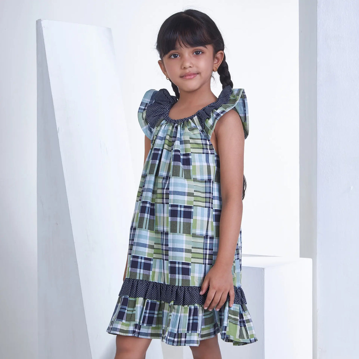 Side pose of a girl wearing patch printed fabric dress in tones of navy, turquoise and green adorned with flutter sleeves