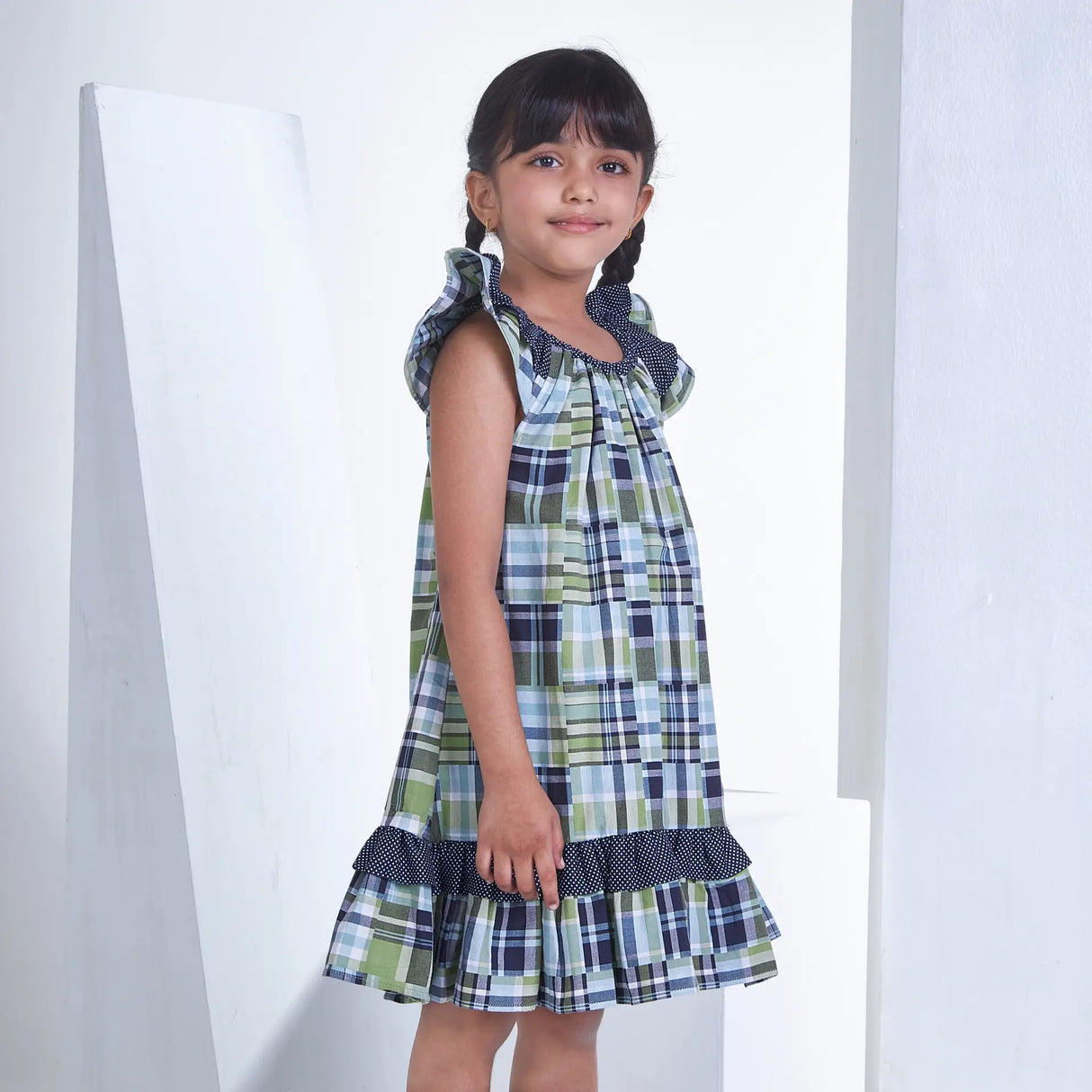 Side pose of a girl dressed in patch printed fabric dress in tones of navy, turquoise and green adorned with flutter sleeves
