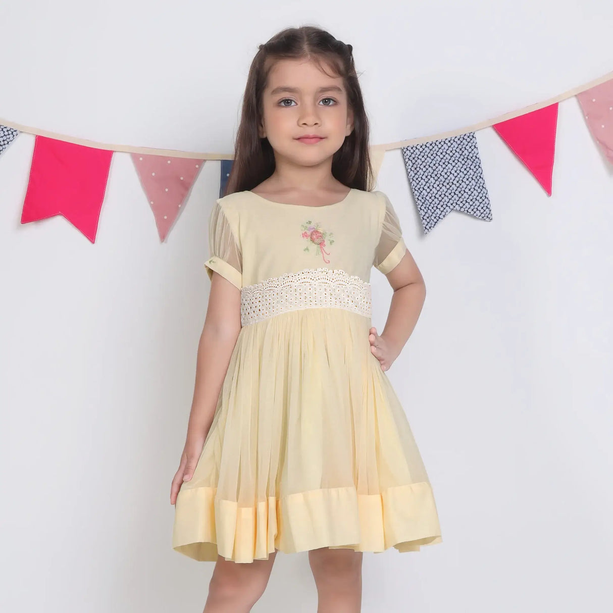 "A little girl with her hand on her hip, dressed in a yellow hand-embroidered tulle dress."