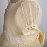 "Close-up of the floral hand embroidery on the puff sleeve of a yellow tulle dress."