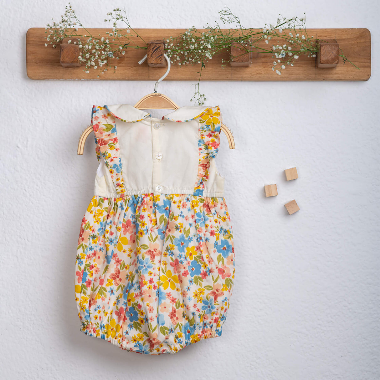 Back view of an ivory floral printed baby girl onesie, fastened with buttons from Soleilclo.