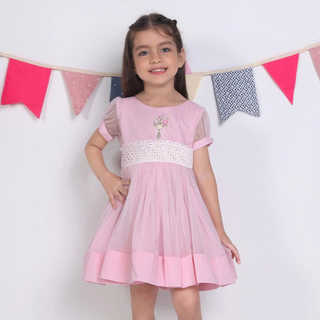 "A little girl with her hand on her hip, dressed in a pink hand-embroidered tulle dress."