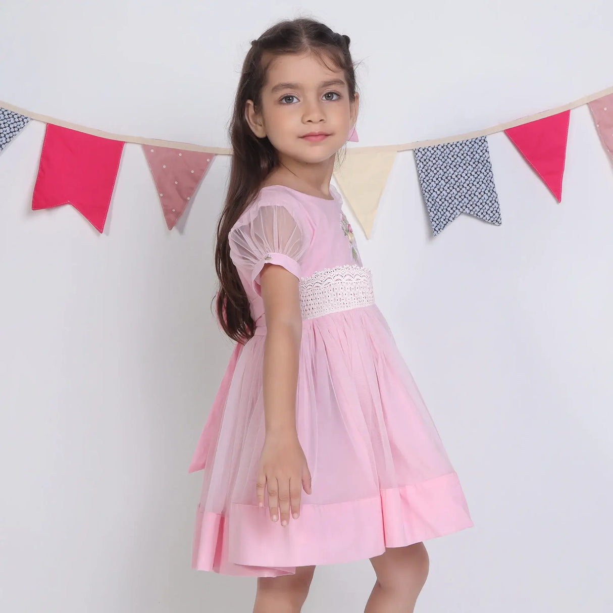 "Side view of a girl in a pink hand-embroidered tulle dress."