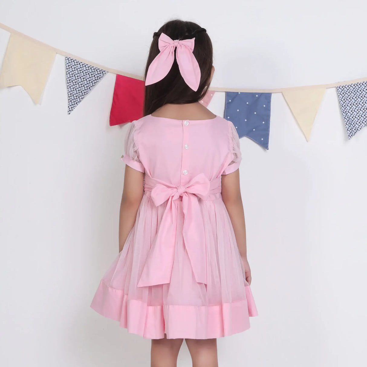 "Back view of a girl in a pink hand-embroidered tulle dress, fastened with buttons and ties."