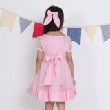 "Back view of a girl in a pink hand-embroidered tulle dress, fastened with buttons and ties."