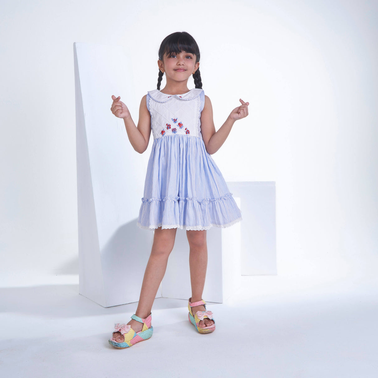 A little girl posing in blue striped embroidered collared dress adorned with ruffled hem