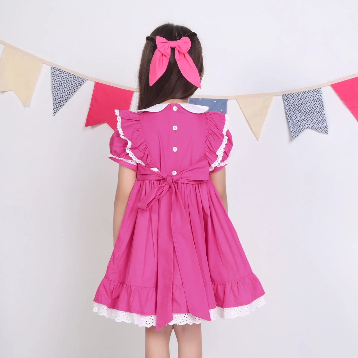 Back view of a girl in a pink embroidered cotton puffed sleeves dress.