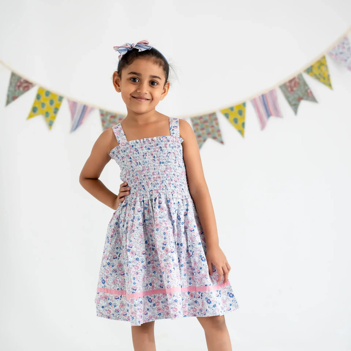 A little girl dressed in a white floral printed strappy dress, with her hand on her hip.