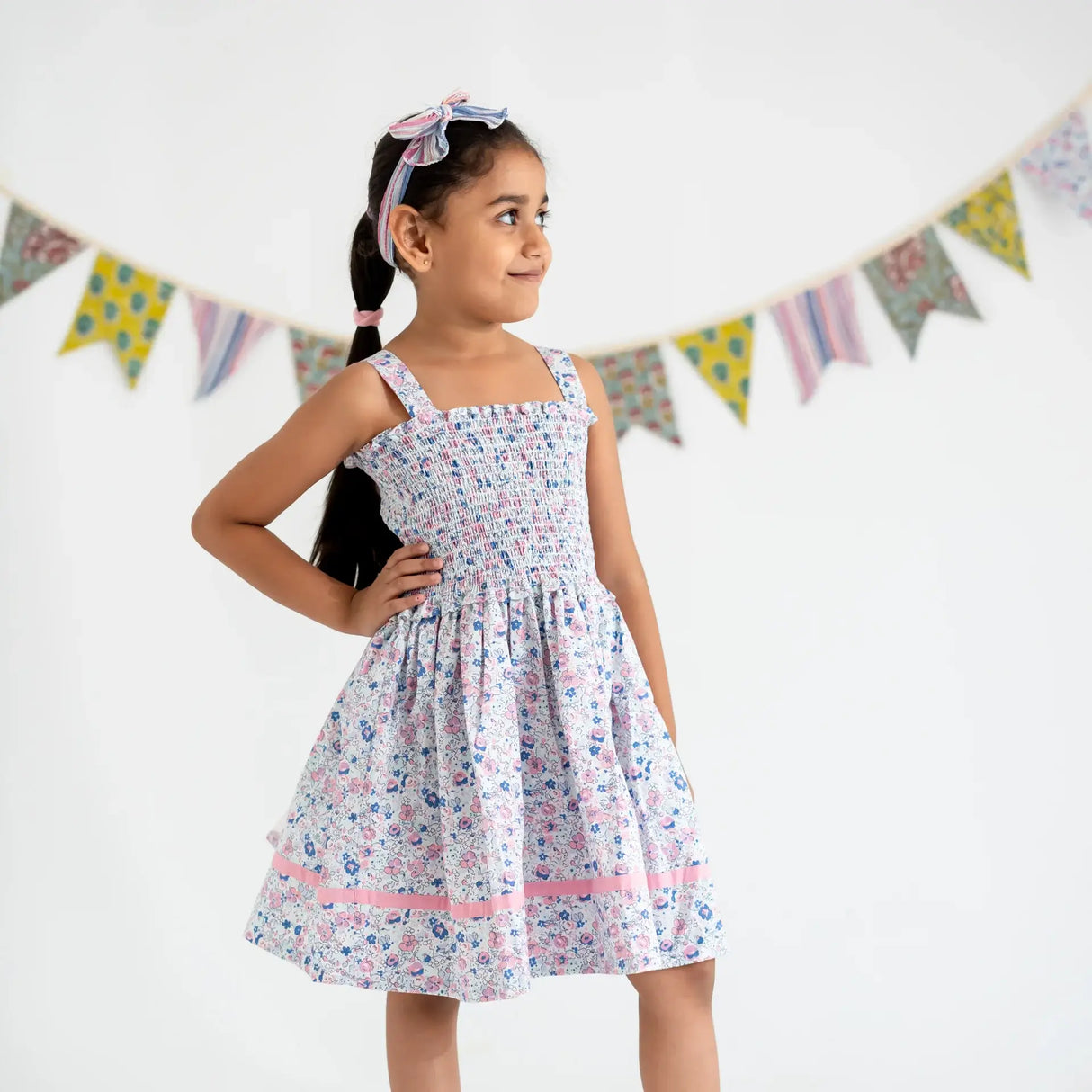 A little girl dressed in a white floral printed strappy dress, with her hand on her hip.