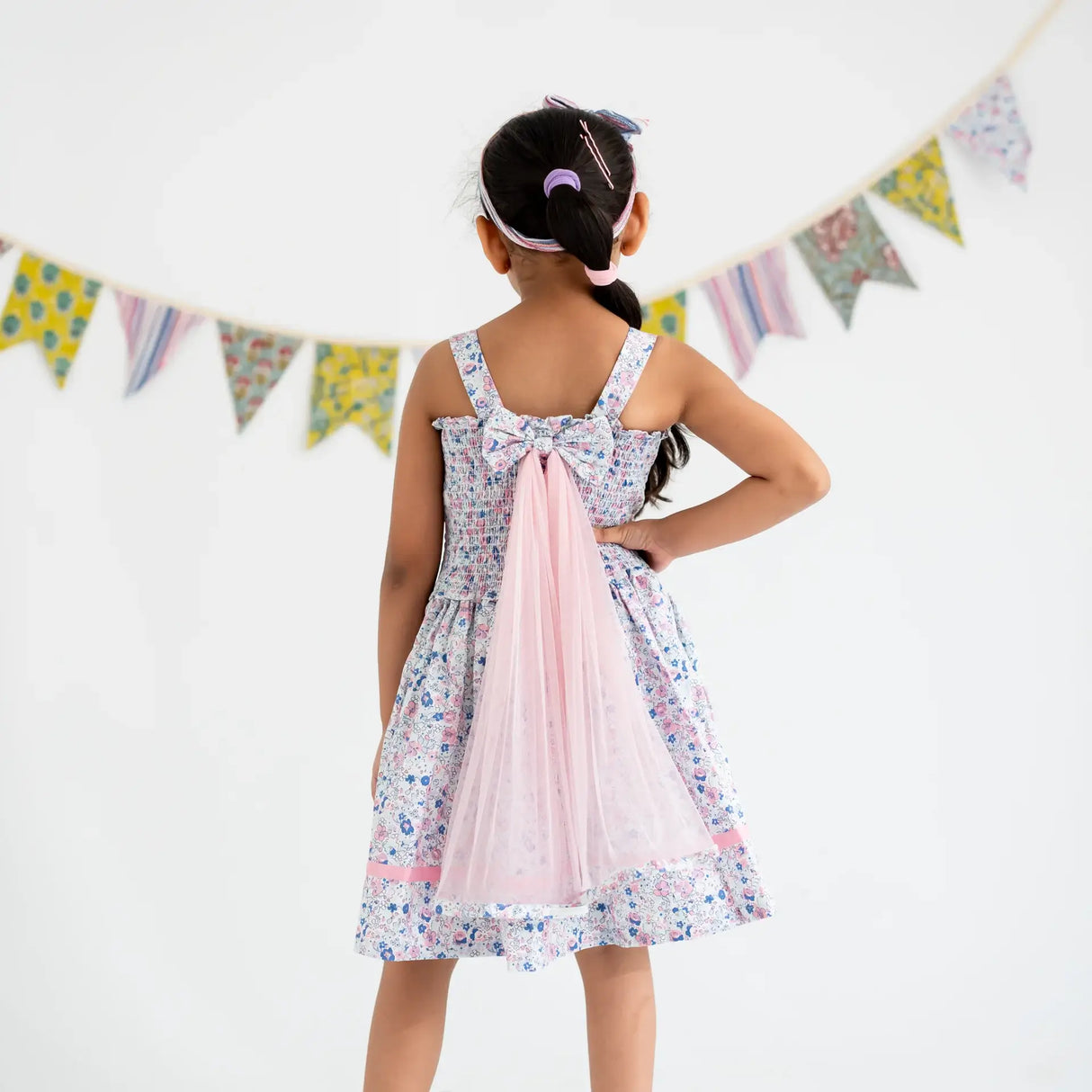 Back view of a girl dressed in a white floral printed strappy dress with attached wings at the back.