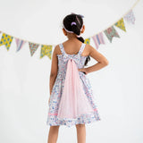 Back view of a girl dressed in a white floral printed strappy dress with attached wings at the back.