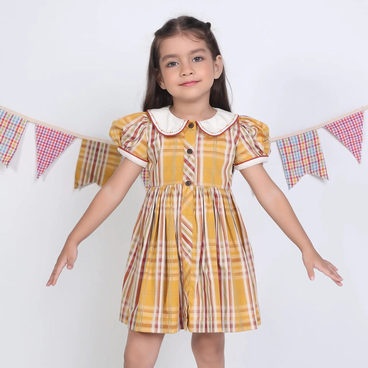 A girl dressed in a mustard checked embroidered cotton puffed sleeves dress.