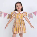 A girl dressed in a mustard checked embroidered cotton puffed sleeves dress.