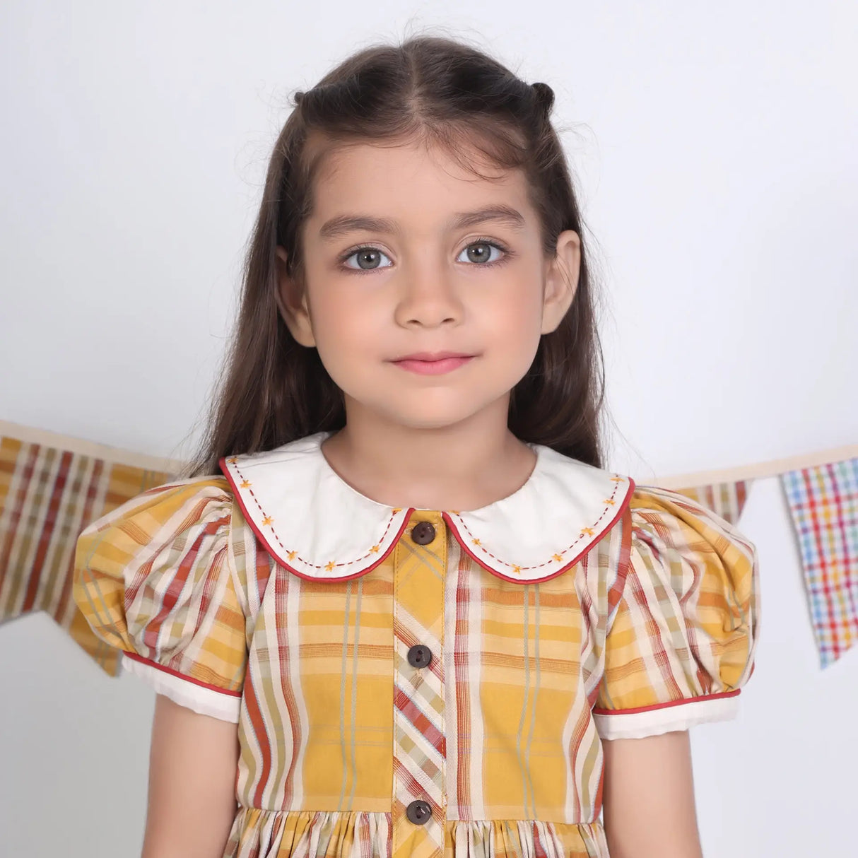 Close-up of a girl in a mustard checked embroidered cotton puffed sleeves dress.