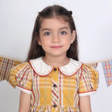 Close-up of a girl in a mustard checked embroidered cotton puffed sleeves dress.
