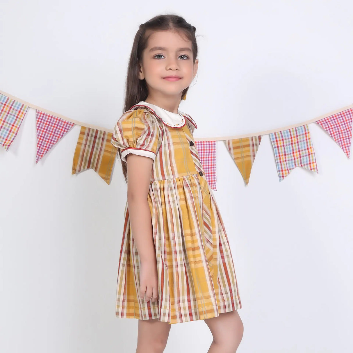 Side view of a girl in a mustard checked embroidered cotton puffed sleeves dress.