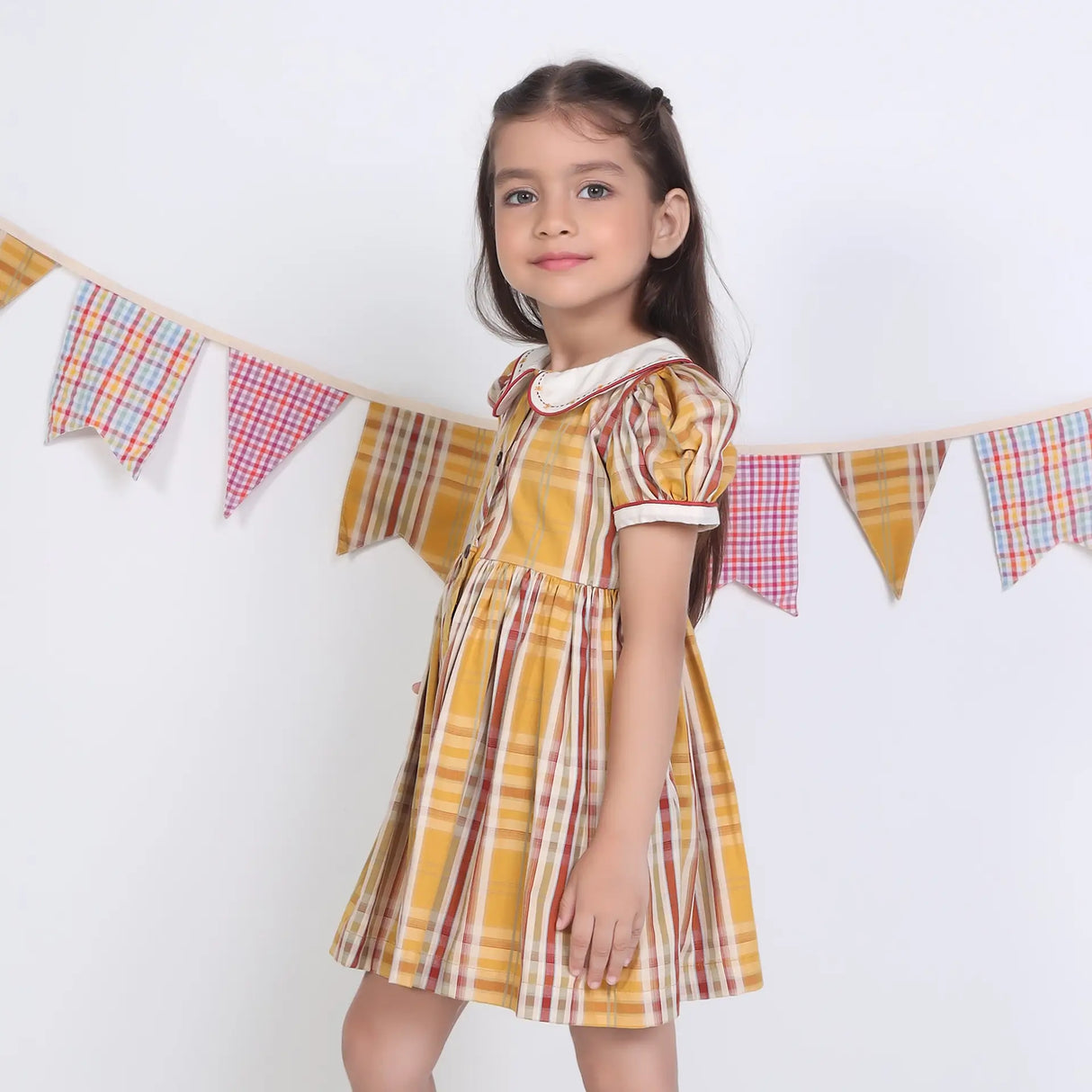 Side view of a girl in a mustard checked embroidered cotton puffed sleeves dress.