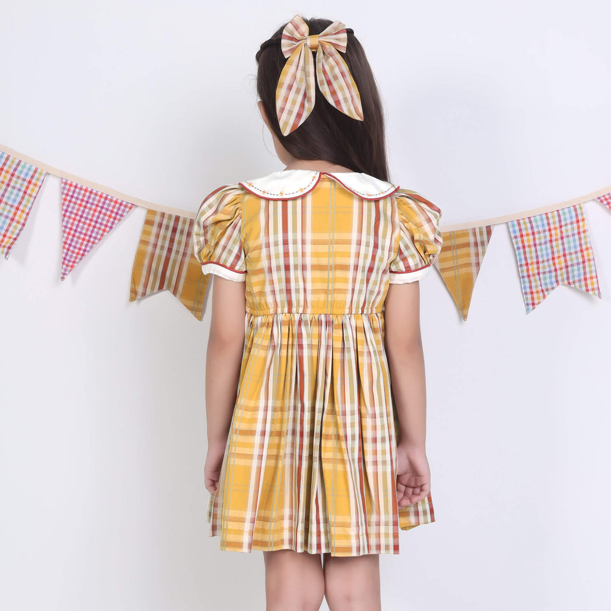 Back view of a girl in a mustard checked embroidered cotton puffed sleeves dress.
