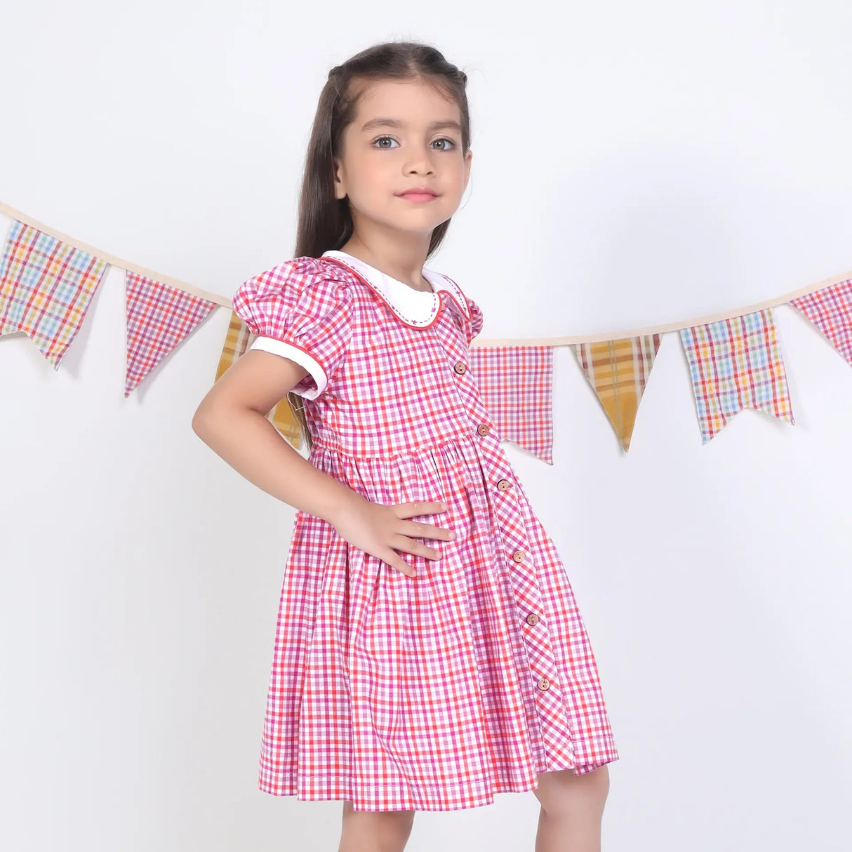 Side pose of a girl in a pink checked embroidered cotton puffed sleeves dress.