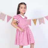 Side pose of a girl in a pink checked embroidered cotton puffed sleeves dress.