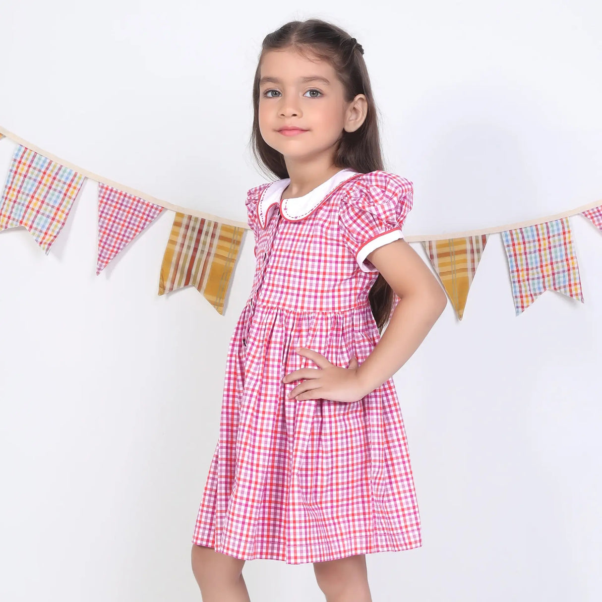 Side pose of a girl in a pink checked embroidered cotton puffed sleeves dress.