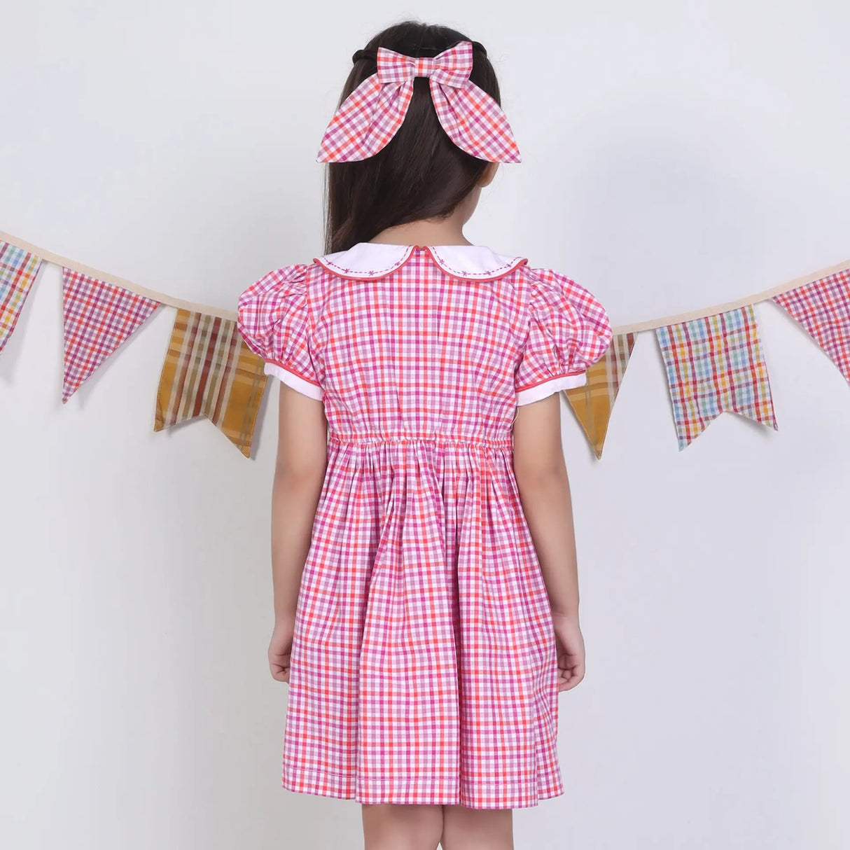 Back pose of a girl in a pink checked embroidered cotton puffed sleeves dress.