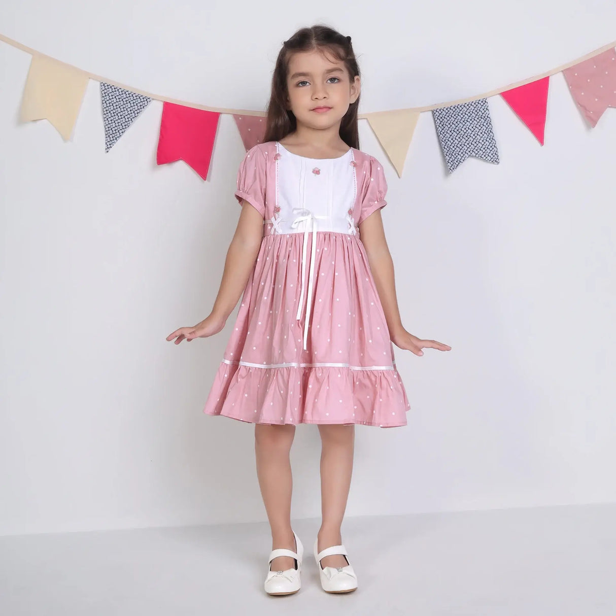 "A little girl posing in a pink embroidered cotton dot printed dress."