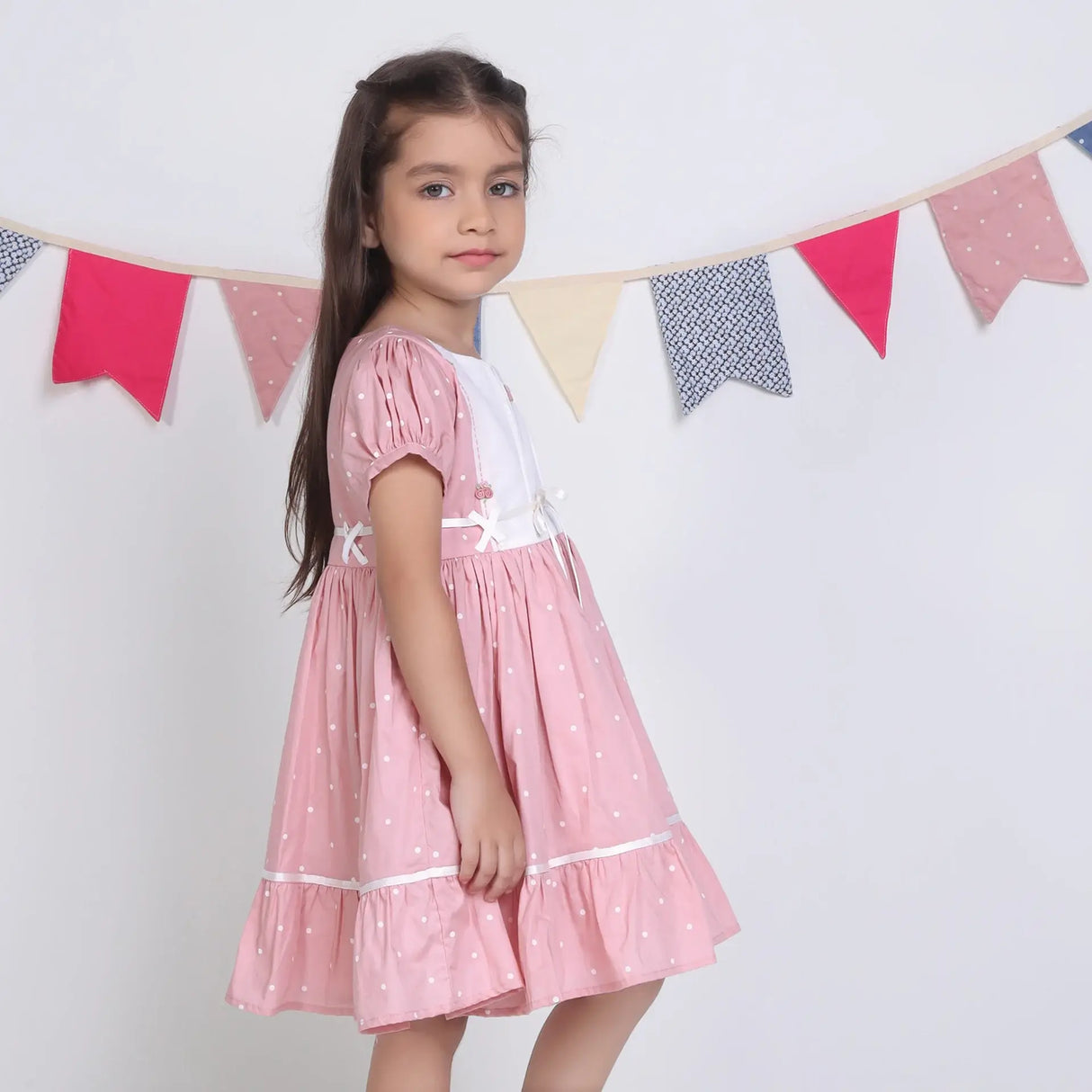 "Side pose of a girl dressed in a pink embroidered cotton dot printed dress."