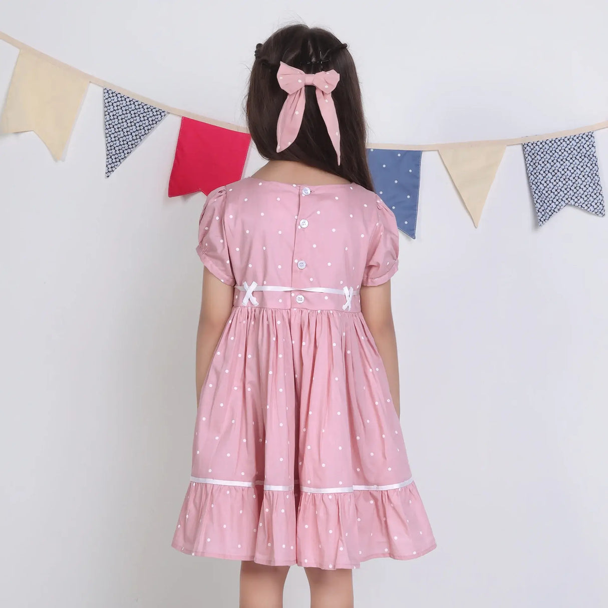 "Back pose of a girl dressed in a pink embroidered cotton dot printed dress."
