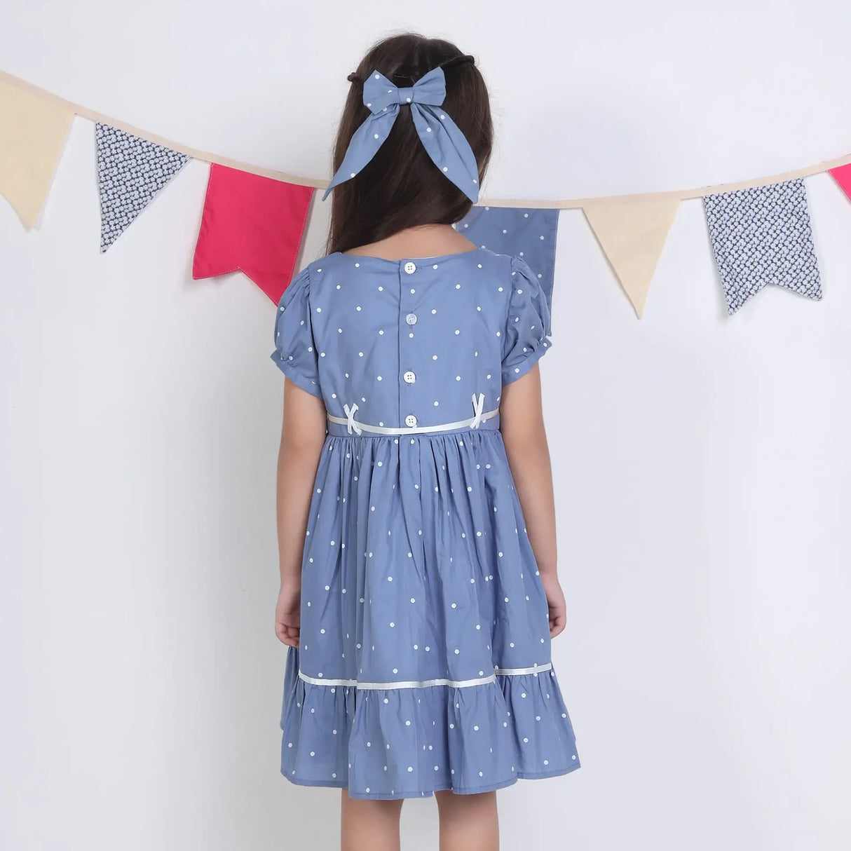 "Back pose of a girl dressed in a blue embroidered cotton dot printed dress."
