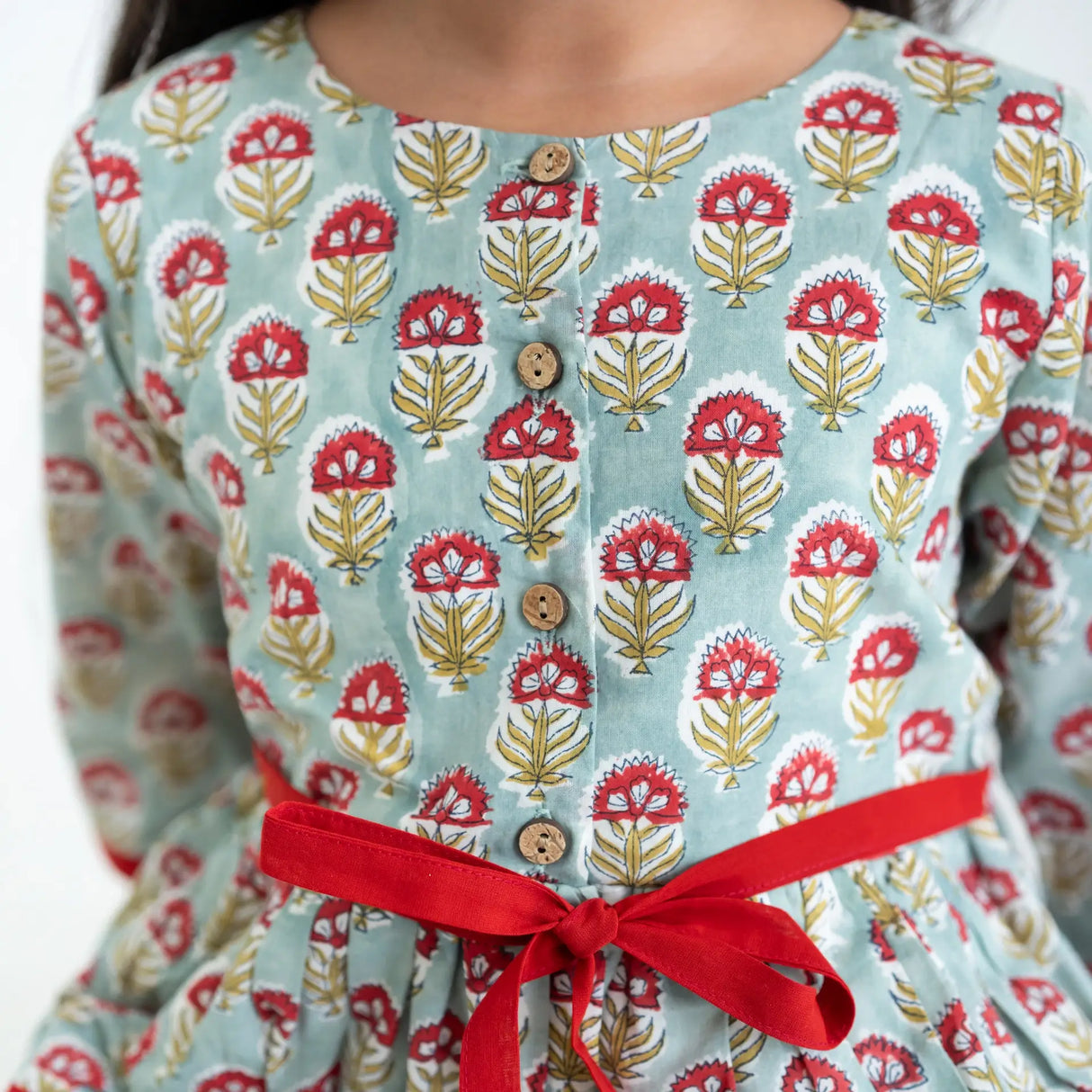 Close-up of a girl dressed in a blue and red printed long sleeves cotton dress with contrast trims.