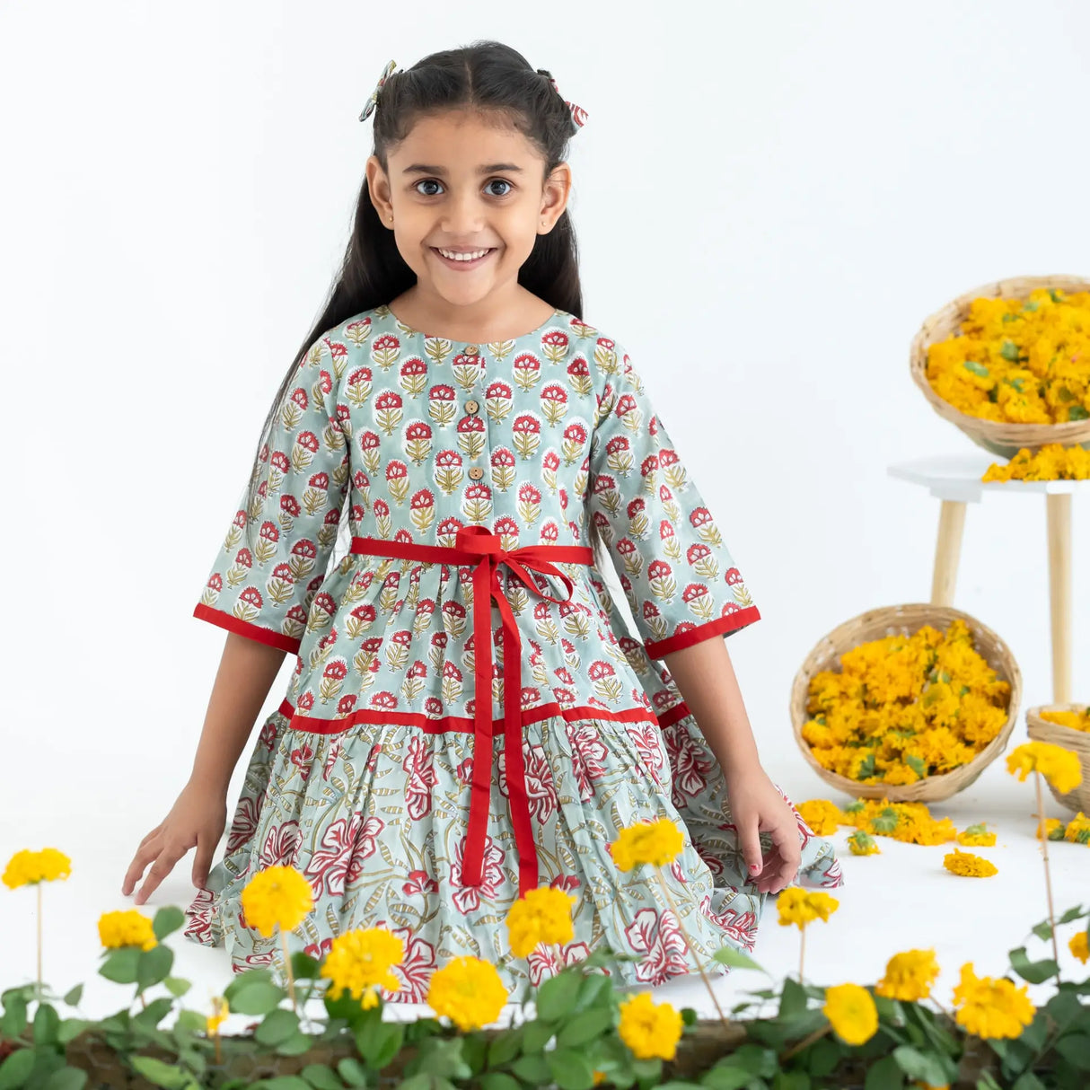 A girl seated, wearing a blue and red printed long sleeves cotton dress with contrast trims.