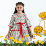 A girl seated, wearing a blue and red printed long sleeves cotton dress with contrast trims.