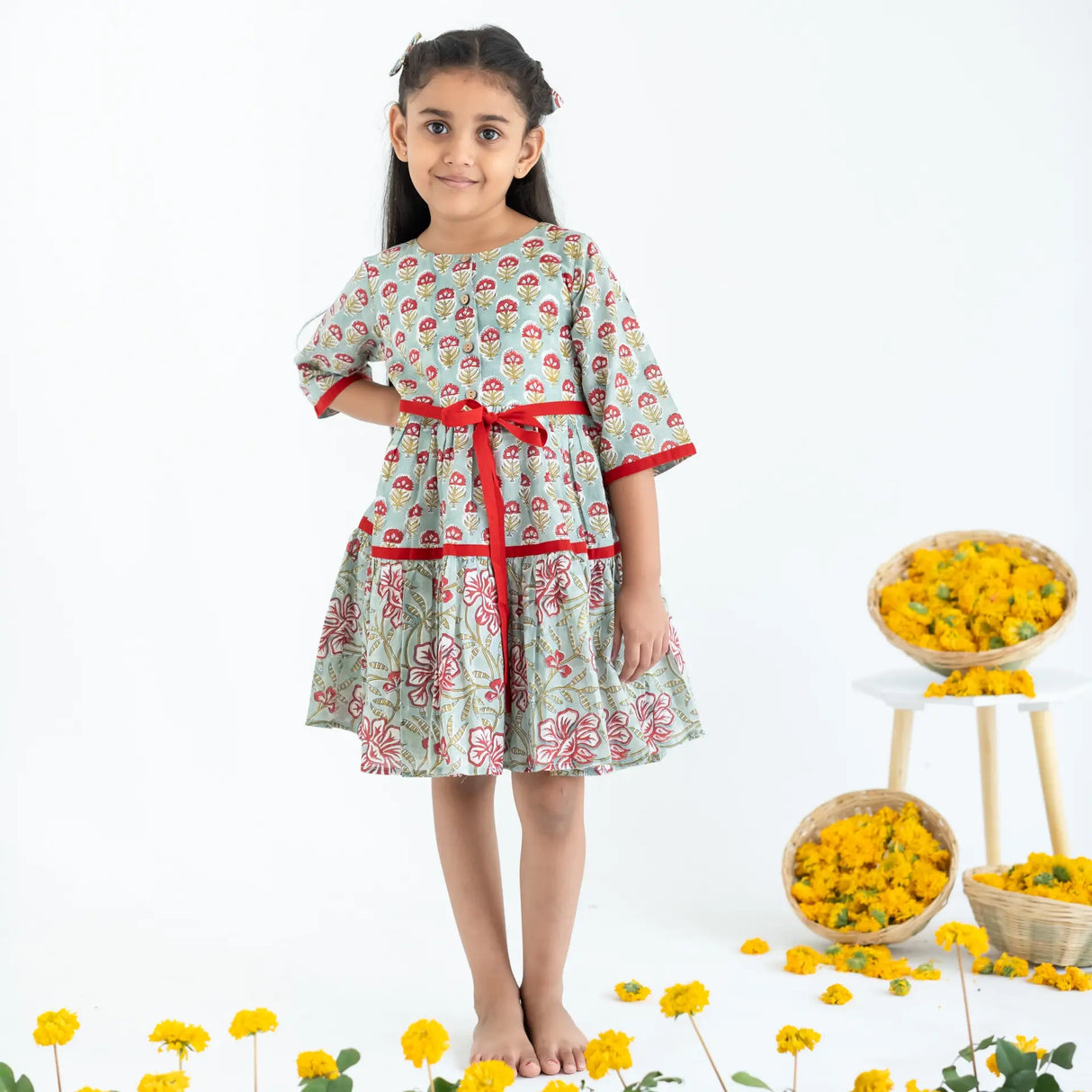 A girl dressed in a blue and red printed long sleeves cotton dress with front opening buttons and ties.
