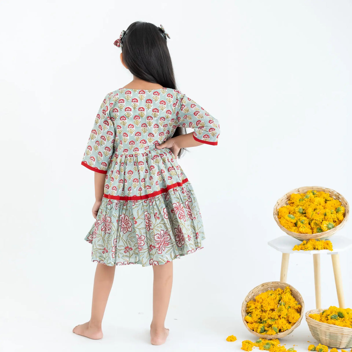 Back view of a girl dressed in a blue and red printed long sleeves cotton dress.