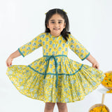 A girl dressed in a yellow and green printed long sleeves cotton dress, stretching the dress with her hands.