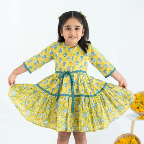 A girl dressed in a yellow and green printed long sleeves cotton dress, stretching the dress with her hands.