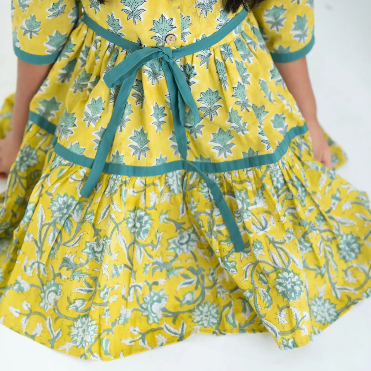 Close-up of a girl dressed in a yellow and green printed long sleeves cotton dress with contrast trims.