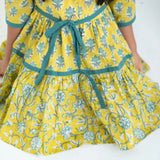 Close-up of a girl dressed in a yellow and green printed long sleeves cotton dress with contrast trims.