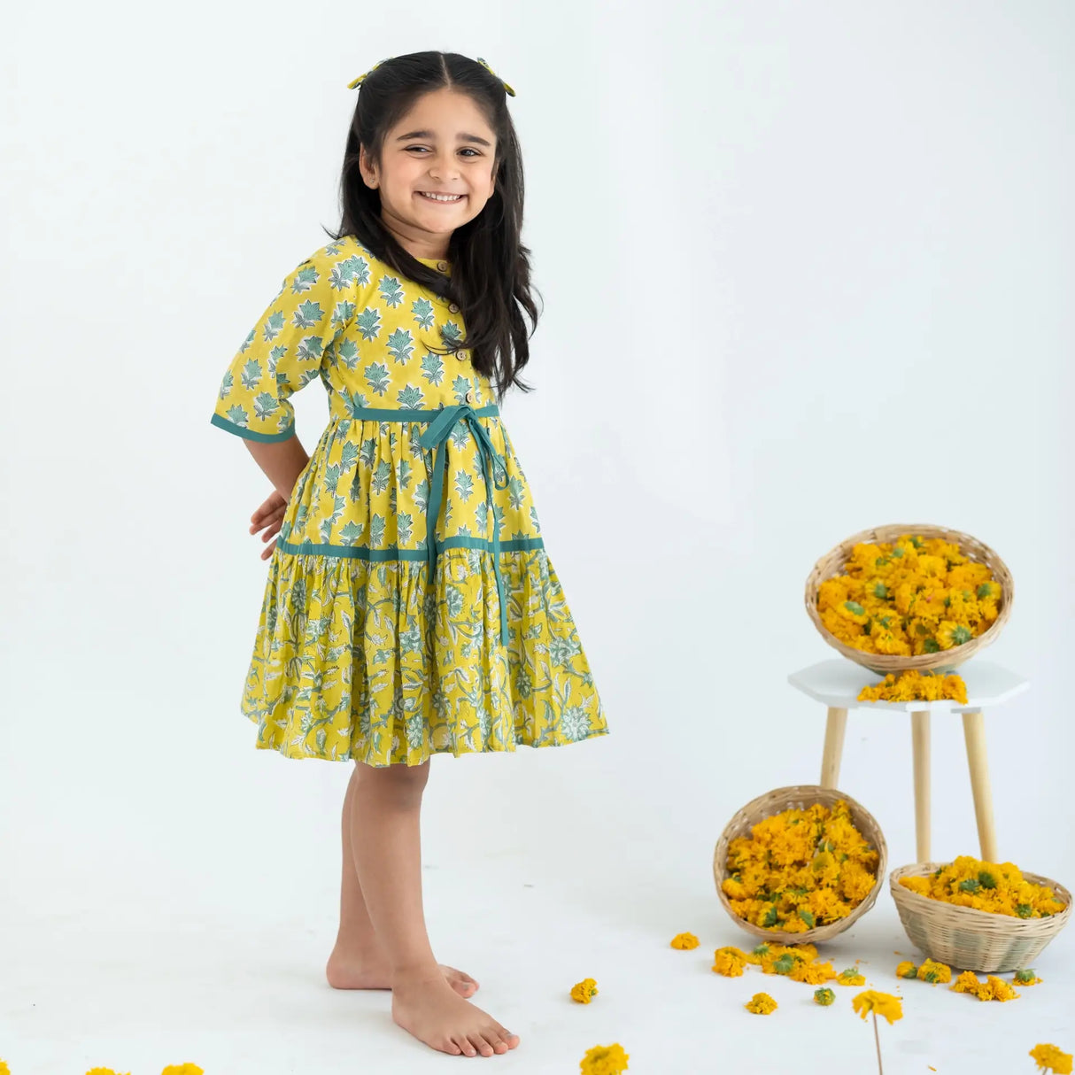 Side view of a girl dressed in a yellow and green printed long sleeves cotton dress with contrast trims.