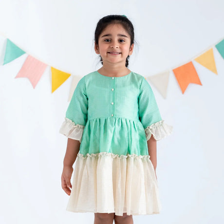 "A girl dressed in a green zari checked cotton silk half sleeves dress."