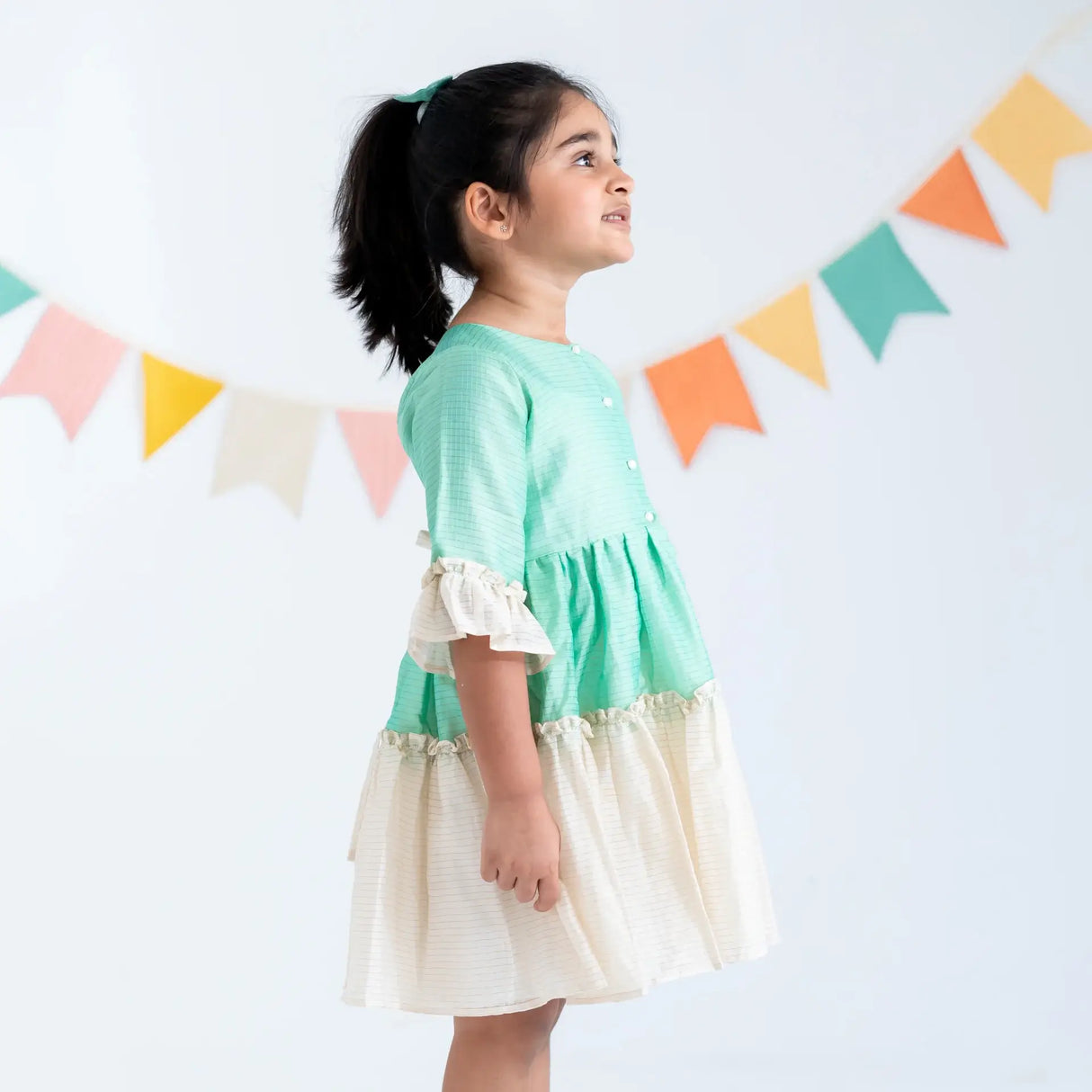 "Side view of a girl in a green zari checked cotton silk half sleeves dress."