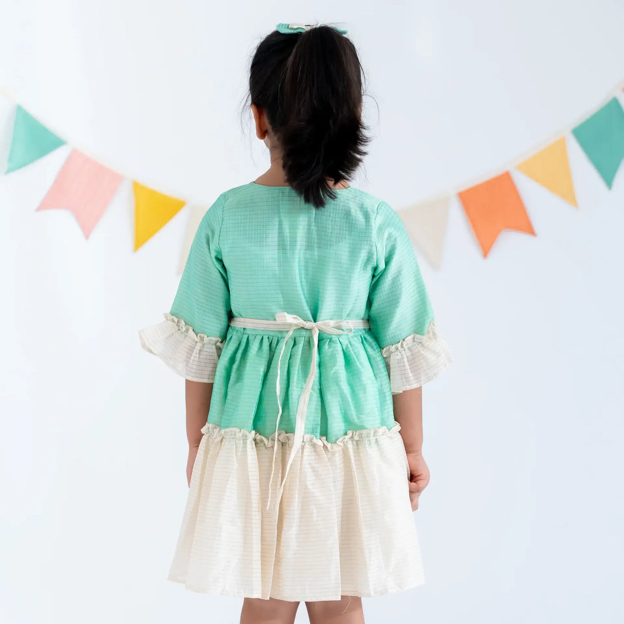 "Back view of a girl in a green zari checked cotton silk half sleeves dress."