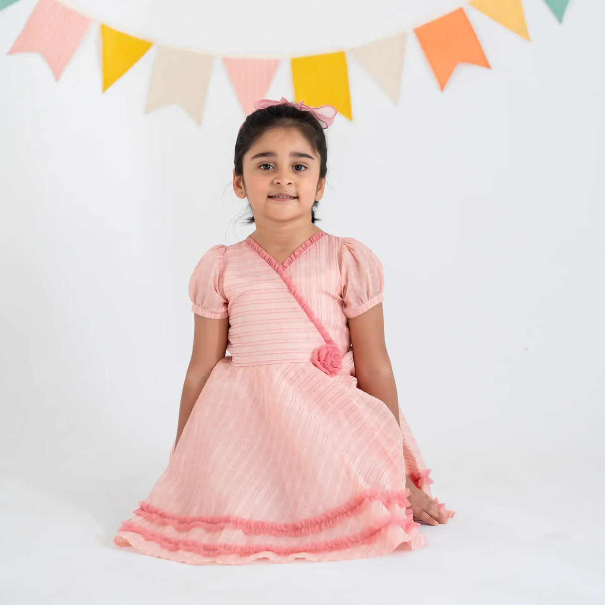 "A girl seated, wearing a pink crossover chanderi puffed sleeves dress."