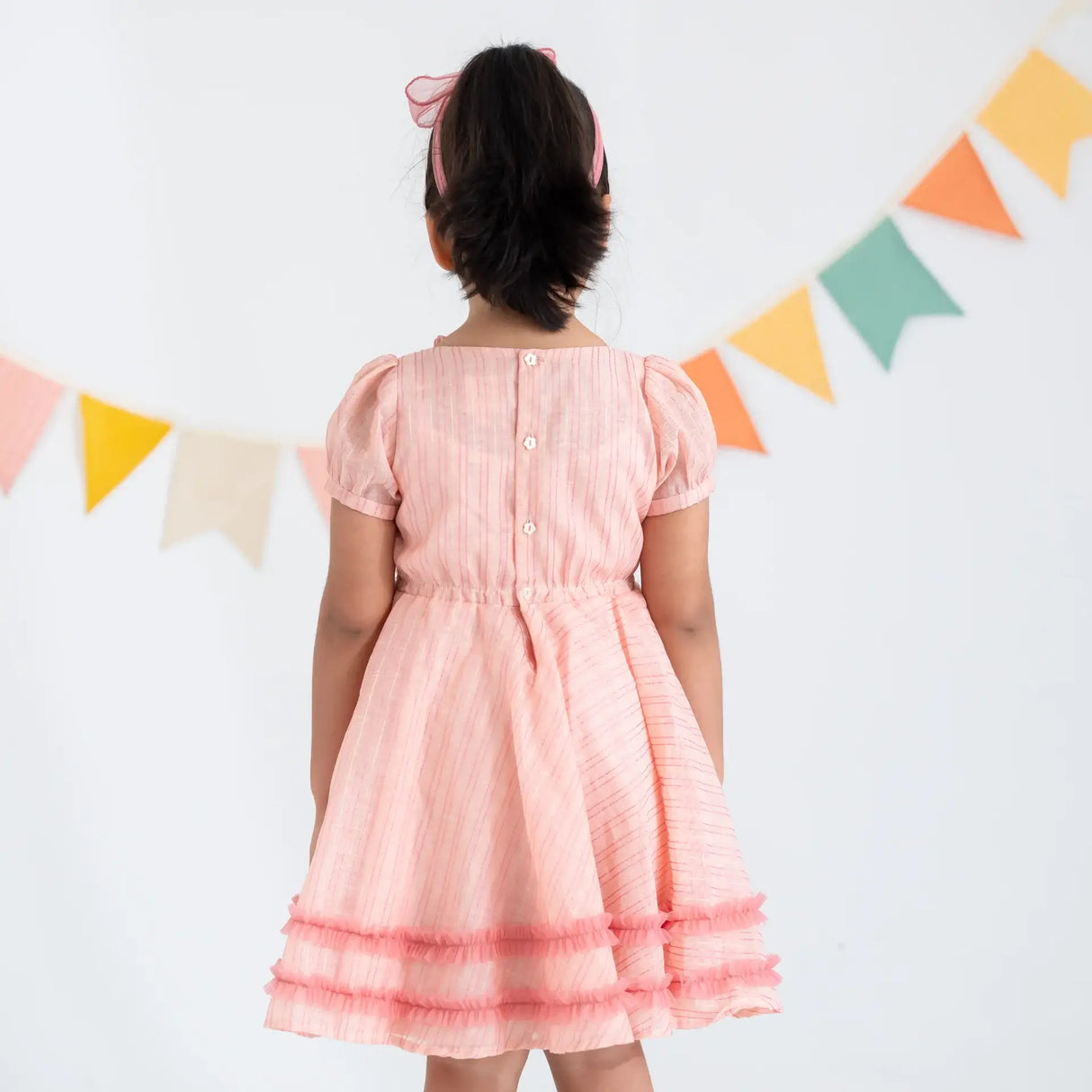 "Back view of a girl in a pink crossover chanderi puffed sleeves dress."